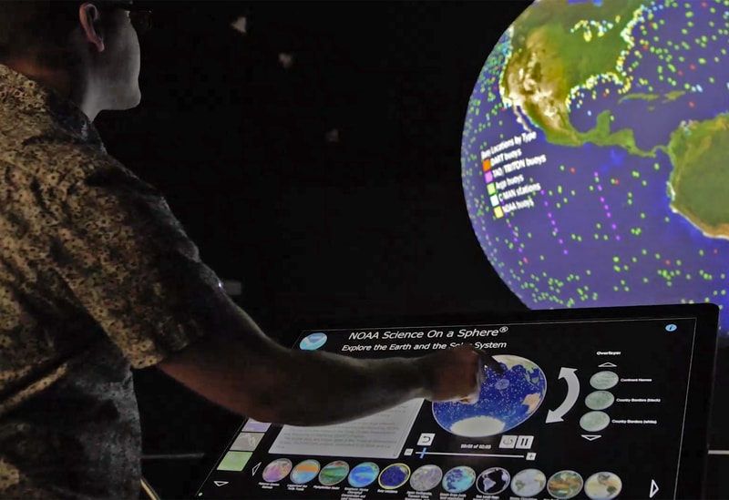 A student interacting with a touchscreen that controls a floating globe demonstrating MSU's commitment to social and cultural studies)