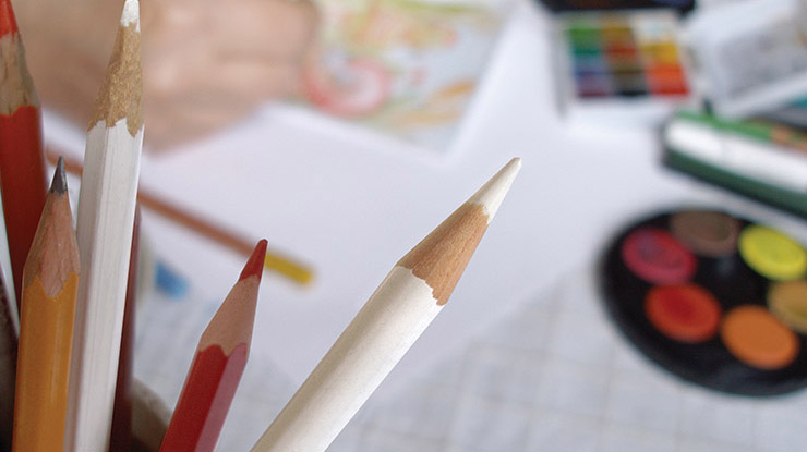 Some art education degree supplies — red and white colored pencils are in sharp focus by multicolored art supplies.