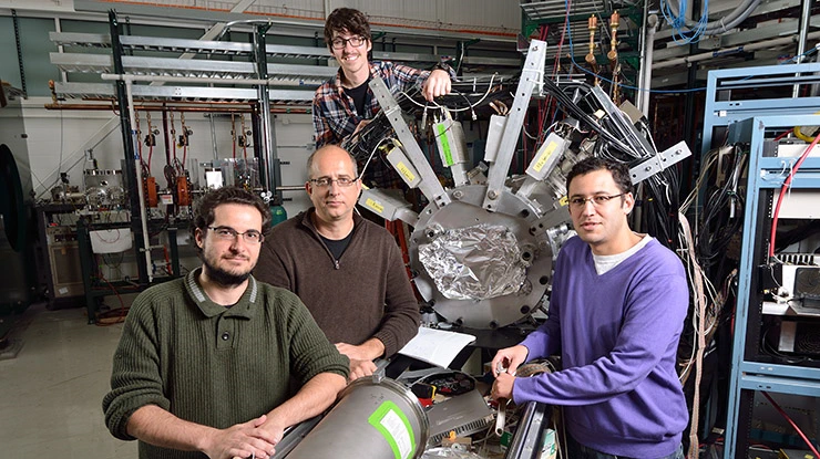 Students pursuing an astrophysics degree and a professor pose in front of equipment used for astrophysics.