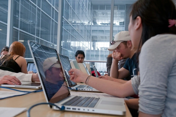 Students pursuing a data science degree work on their laptops and collaborate in an open space, ultramodern building.