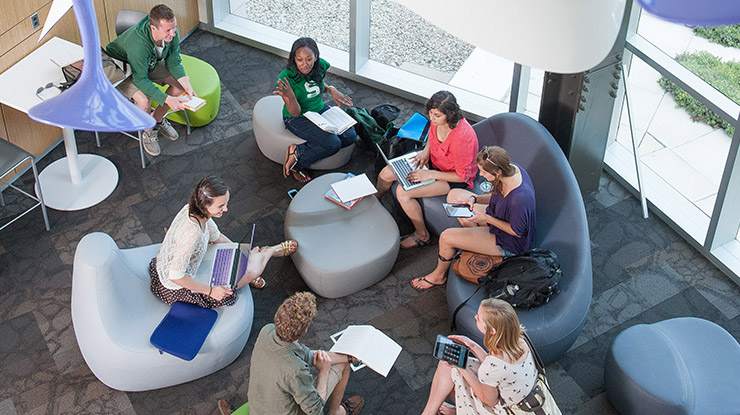Students working on a degree in arts and letters sit in a cluster in a modern study space, smiling and talking.