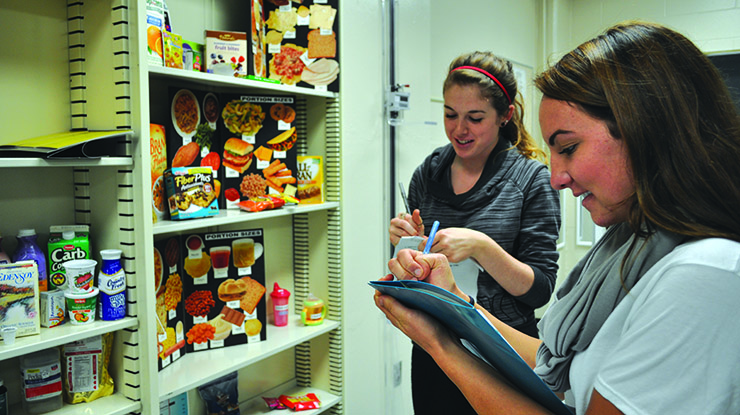 Two students working for their dietetics degrees stand in front of shelves of colorful displays of labeled food information.