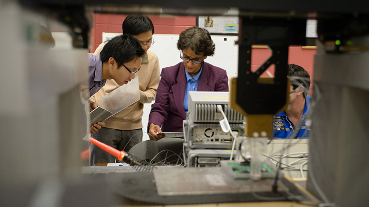 A professor demonstrates on classroom equipment to a small group of students pursuing an electrical engineering degree.