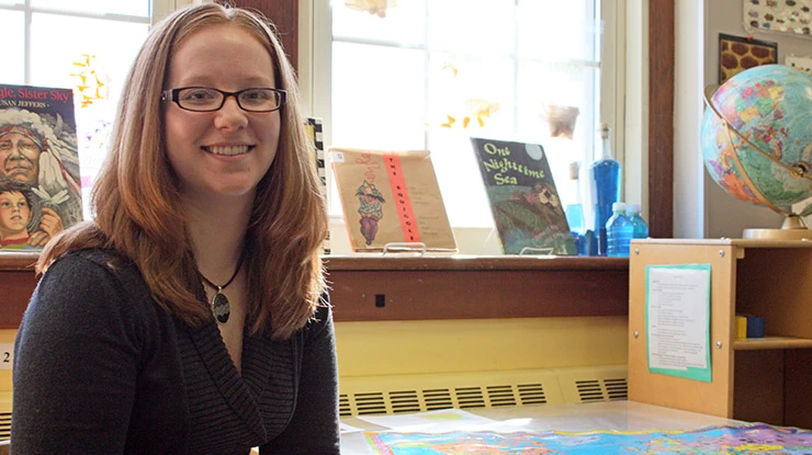 A human development and family studies major smiles and sits at a table surrounded by children’s books and a globe.