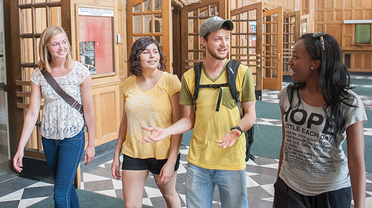 A group of smiling humanities majors walk side by side down a hallway in a building on MSU’s campus.