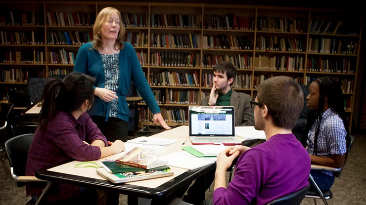 A professor instructs a small table of James Madison College majors in front of a wall of packed bookshelves.