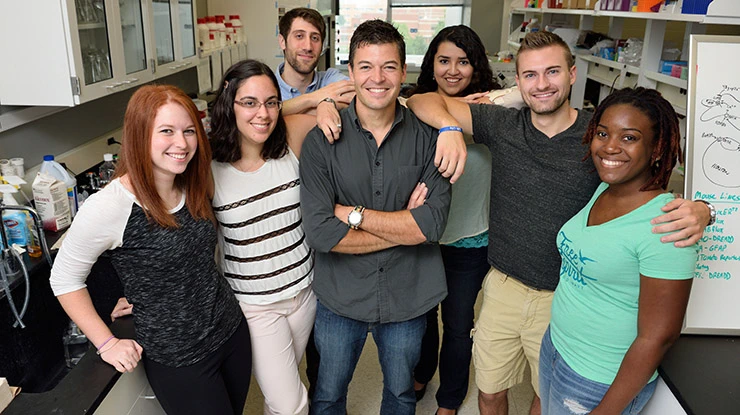 In a lab, a group of friendly, smiling neuroscience majors put their arms around each other and take a group photo.