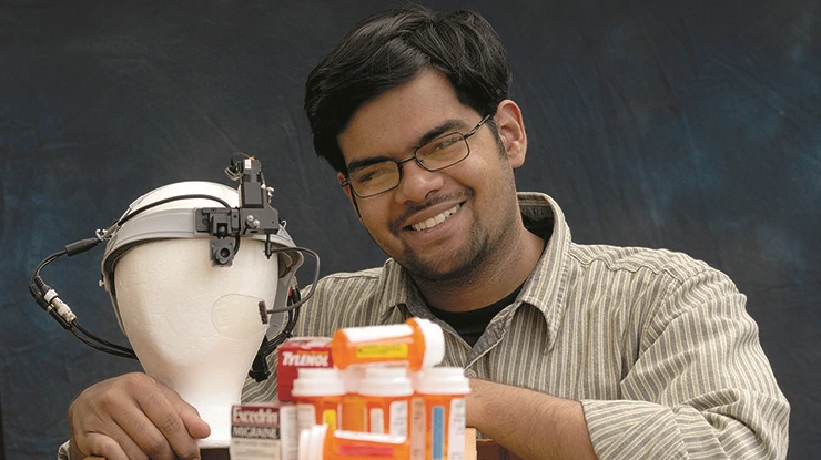 A smiling packaging major sits next to a mannequin head wearing a device, pill bottles and boxes of Tylenol and Excedrin.