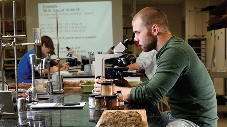A student in a plant and soil science class looks into a microscope and works on an assignment on the classroom projector.