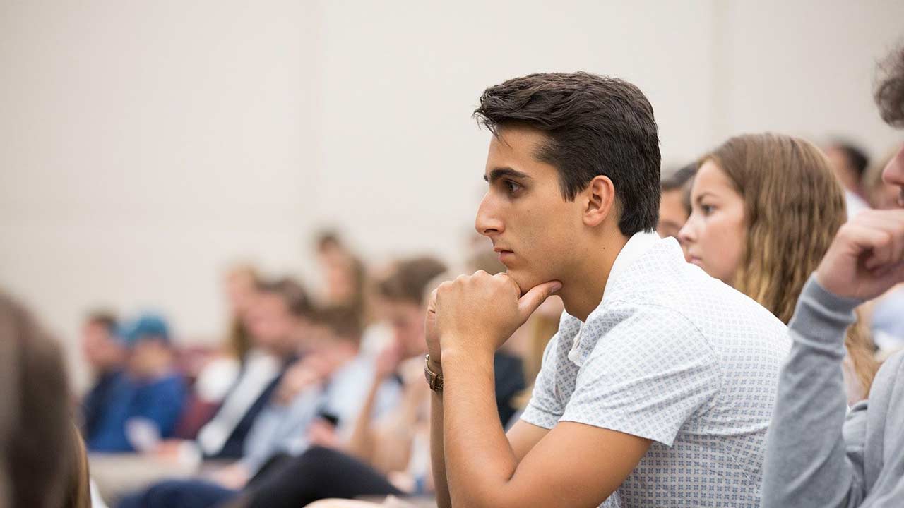 In a crowded classroom of students working on a supply chain management degree, one student sits forward listening intently.