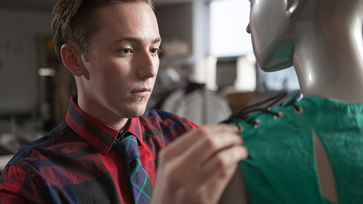 A textile and apparel student makes an adjustment to a top on a mannequin.