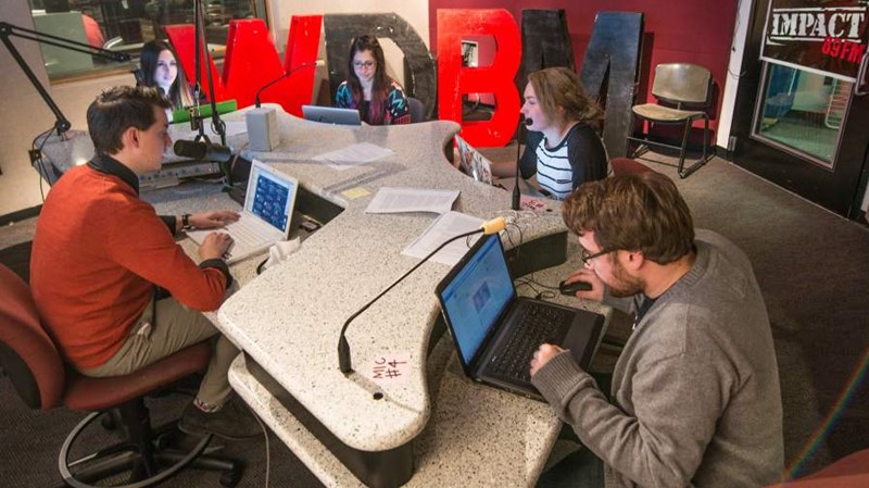 Five students working in a broadcasting studio at Impact 89FM, a student radio station that offers student employment.