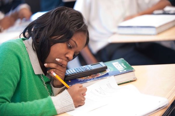 A student in a green sweater leans over a desk as she takes notes on a piece of paper