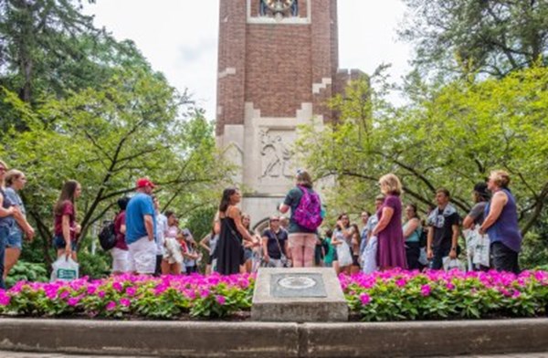 An MSU campus tour group gathered around the Beaumont tower listens to a student tour guide