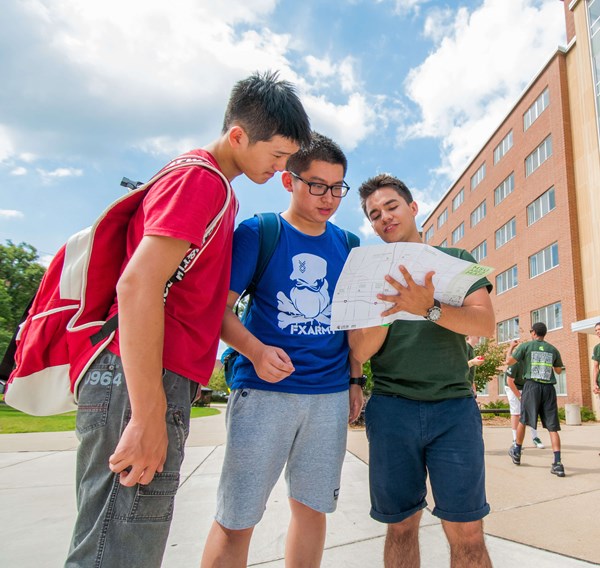 A group of three students stand in front of a residence hall on Michigan State University's campus and read a campus map